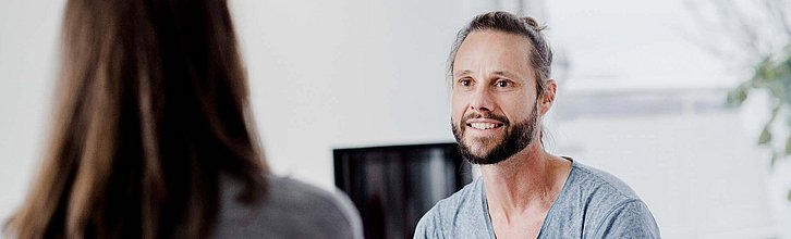 Zwei Menschen miteinander im Gespräch, eine Person ist nur von hinten zu sehen